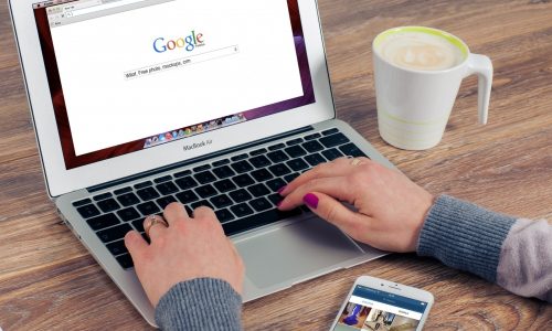 woman-working-on-laptop-with-mobile-phone-and-coffee-cup-on-table