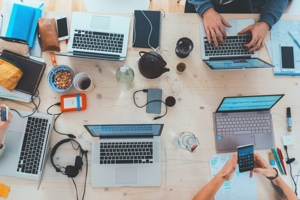 five laptops on a table with one person working and the other on their phone